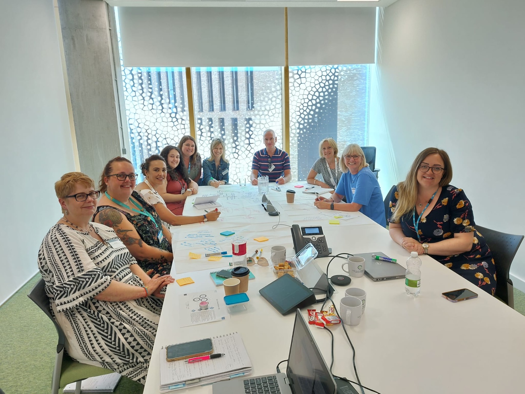 A group of people who are part of the Cancer Alliance sat at a table and looking at the camera smiling